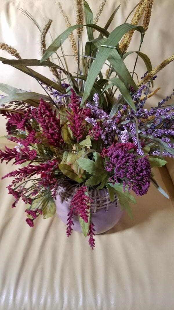 A Fall Floral arrangement in a vase on a couch.