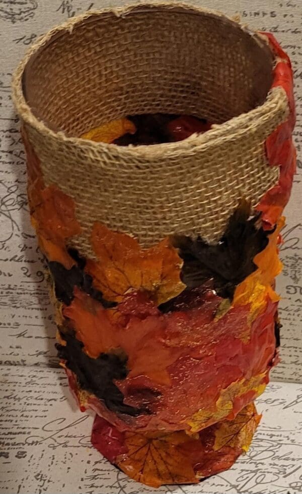 A glass jar decorated with burlap and fall leaves.