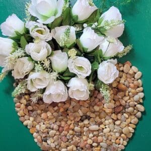 White roses in a heart-shaped vase of pebbles.