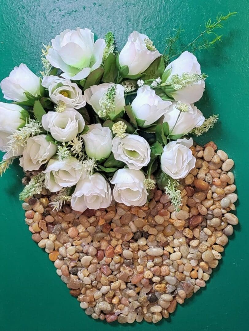 White roses in a heart-shaped vase of pebbles.