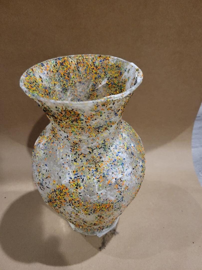 A tall, plastic vase with multi-colored confetti pieces.