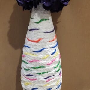 A yarn-wrapped bottle vase with purple flowers.