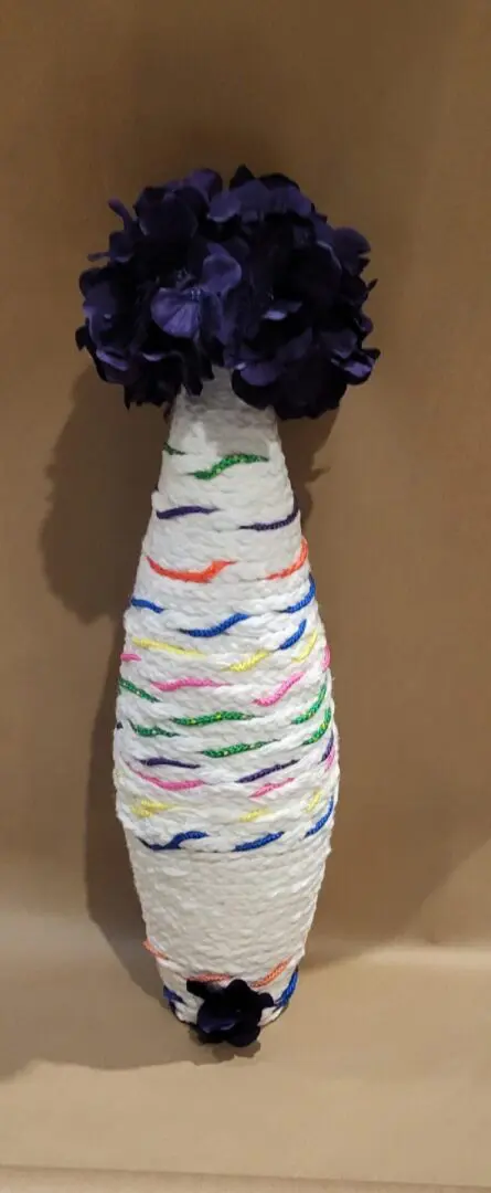 A yarn-wrapped bottle vase with purple flowers.